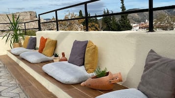 Un espace de détente aménagé sur le toit, avec un mur en pierre en arrière-plan, un pot de fleurs et une vue sur un paysage montagneux.