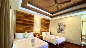 Habitación de hotel con dos camas, cabeceros de madera, un ventilador de techo y un cuadro en la pared.
