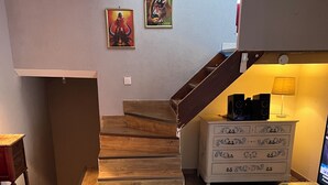 Uma sala de estar com escada de madeira, mesa de centro de vidro, sofá vermelho e cômoda branca com padrões decorativos.