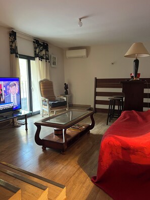 A living room with a glass-top coffee table, a red sofa, a wooden chair, a TV, and a lamp.