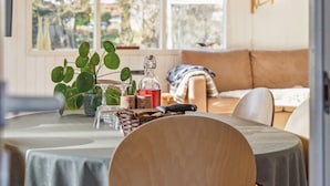 A cozy dining area with a round table, chairs, a hanging light fixture, a window with a view of trees, and a sofa in the background. - "Ristana" - 200m from the sea by Interhome (Ebeltoft)