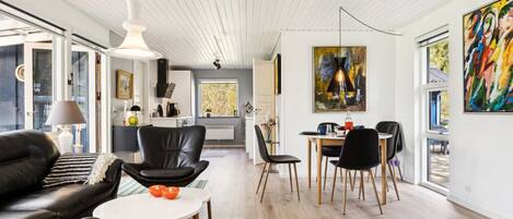 Een moderne woonkamer met een zwarte leren bank, een ronde eettafel met stoelen en een keuken op de achtergrond.