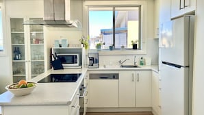 A modern kitchen with white cabinets, a stainless steel refrigerator, a built-in microwave, and a coffee maker. - Cosy unit with delightful park and water views. Perfect for a family holiday! (BALLINA)