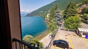 A balcony with a view of a lake, a parking area, and a mountainous landscape.