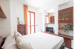Ein Hotelzimmer mit Bett, Schreibtisch mit Computer, Fernseher, Uhr und einem Fenster mit Vorhängen.