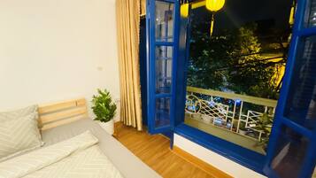 A bedroom with a bed, a window with curtains, a small plant, and a balcony with railings.