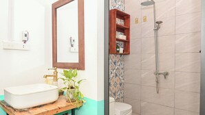 Et badeværelse med en hvid vask, en træhylde med toiletartikler, en bruseniche med håndbruser og et toilet.