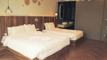 A hotel room with two beds, a wooden floor, a mirror, and a bathroom with a sink.