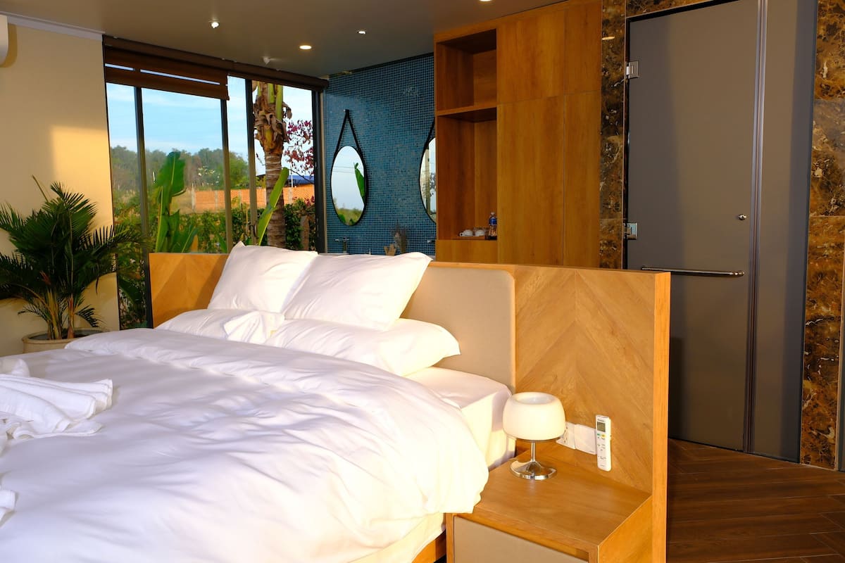 Une chambre d’hôtel moderne avec un grand lit, une table de chevet avec une lampe, une armoire et une vue sur l’extérieur.