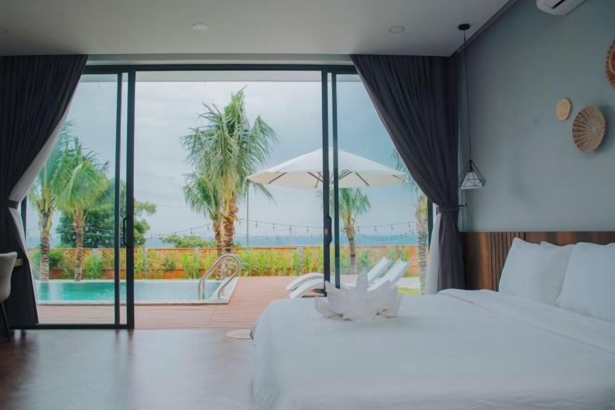 Ein Hotelzimmer mit einem großen Bett, Blick auf einen Pool und Palmen sowie einer Schiebeglastür.