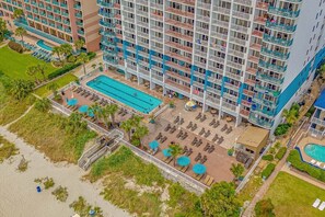 Un hotel moderno de gran altura con varios balcones, una piscina central y una zona de playa con tumbonas.