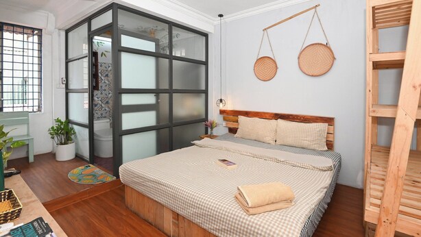 A bedroom with a bed, a wooden bench, a small table with books, a potted plant, and a window with a view. - Apt*2BR  3 Beds in the center for 5 pax-Sunny homestay (Hà Nội)