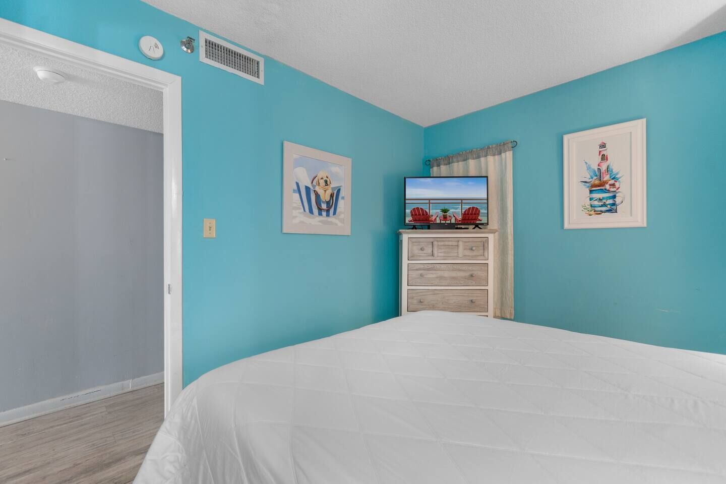 A bedroom with a bed, a dresser, and two wall-mounted TVs.