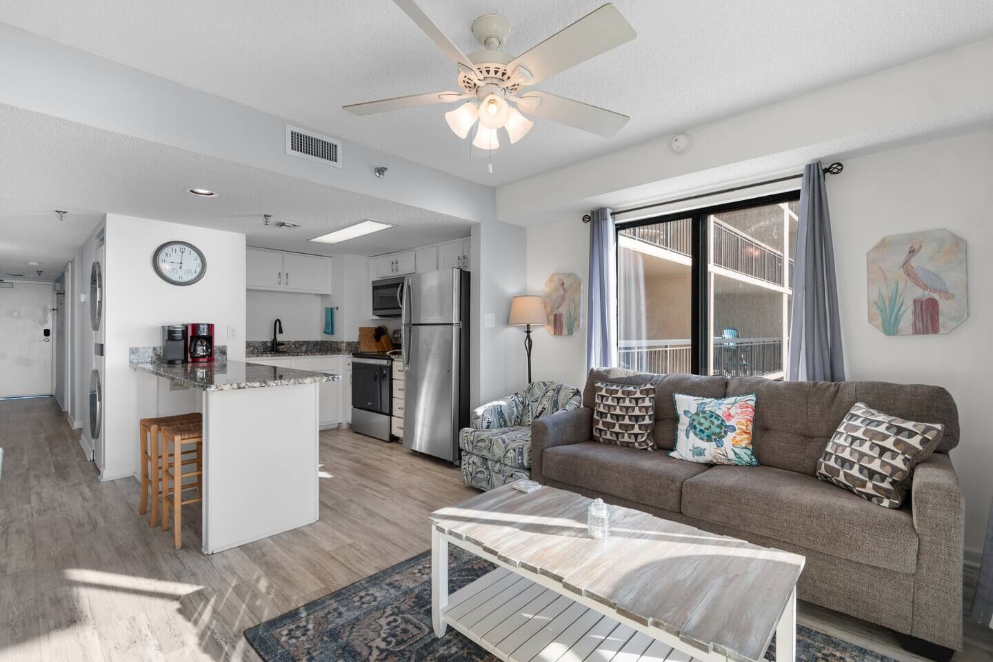 A modern apartment with a kitchenette, a living area with a sofa and coffee table, and a large window with a balcony.