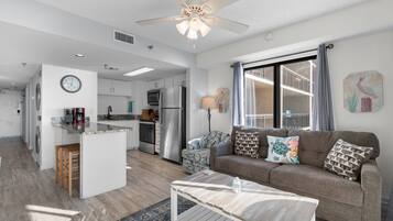 A modern apartment with a kitchenette, a living area with a sofa and coffee table, and a large window with a balcony.