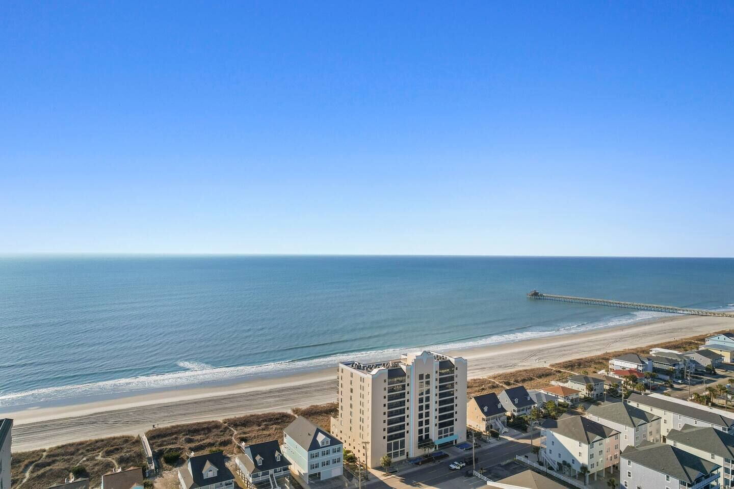 A coastal area with a beach, a pier, and residential buildings.