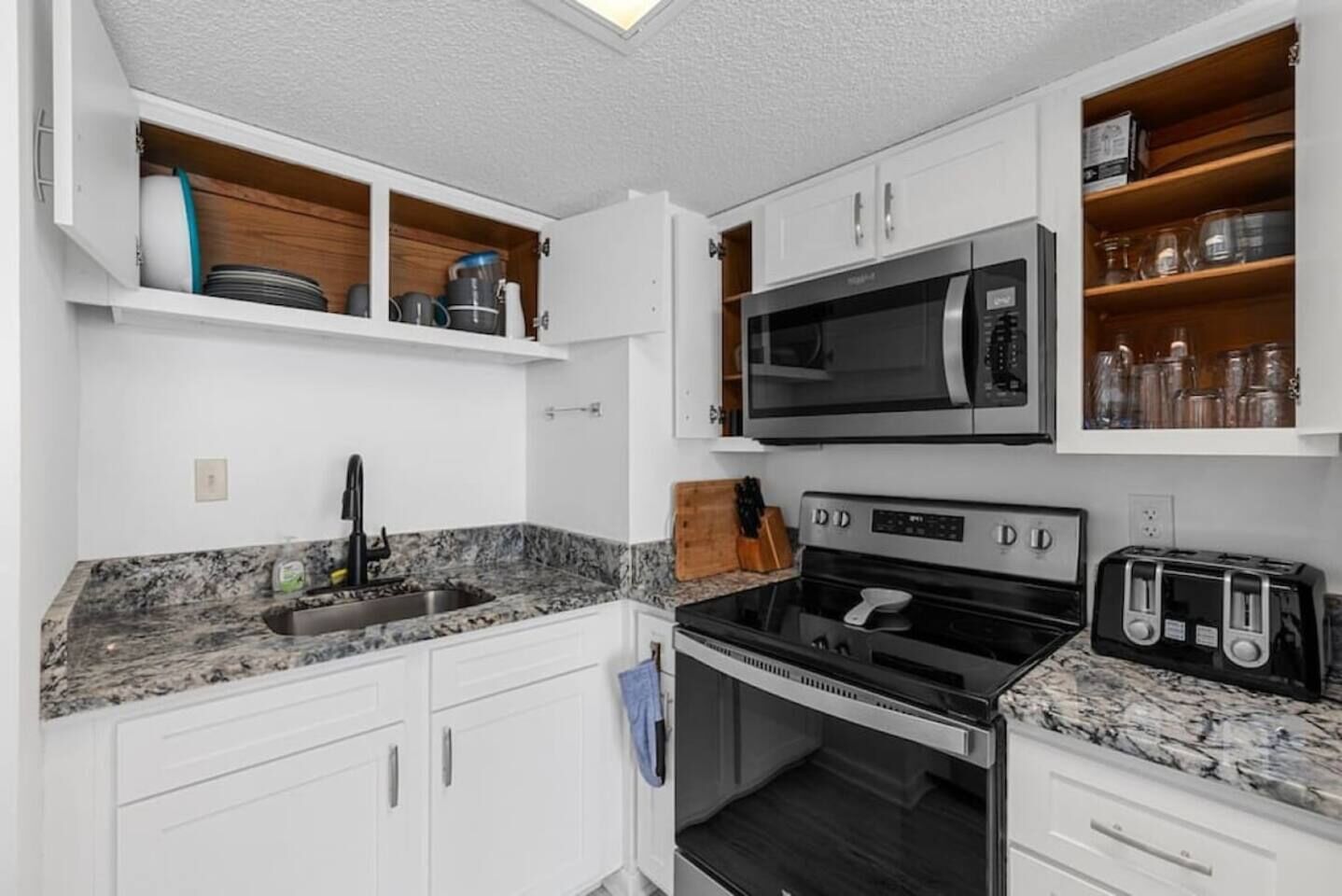 A compact kitchen with white cabinets, a built-in microwave, a stove, and a toaster.