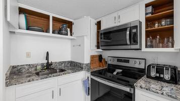 A compact kitchen with white cabinets, a built-in microwave, a stove, and a toaster.