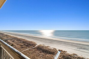 A beach with a clear sky and calm sea, viewed from a balcony.