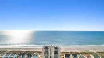 A beachfront hotel with a view of the ocean, featuring multiple-story buildings and a parking area.