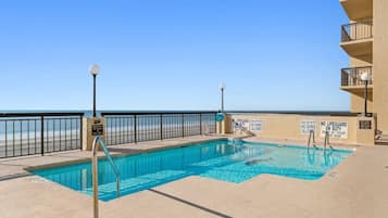 Una piscina con vista a la playa, rodeada por una valla y varios letreros de advertencia.