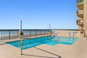 Ein Swimmingpool mit Blick auf einen Strand, umgeben von einem Zaun und mehreren Warnschildern.