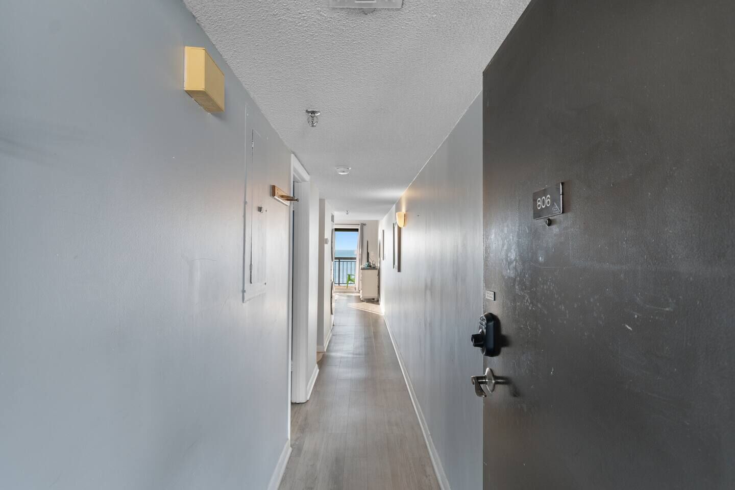 A hallway with a view to a balcony, a door with a number plate, and a light fixture on the wall.
