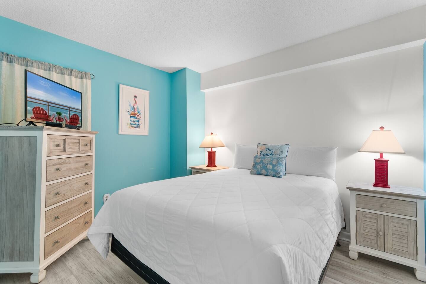 A bedroom with a large bed, two bedside tables with lamps, a dresser, and artwork on the walls.