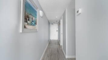 A hallway with a wooden floor, white walls, and a framed picture on the left.