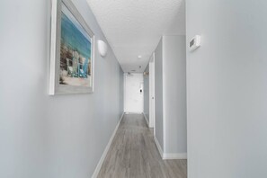 Un pasillo con piso de madera, paredes blancas y un cuadro enmarcado a la izquierda.