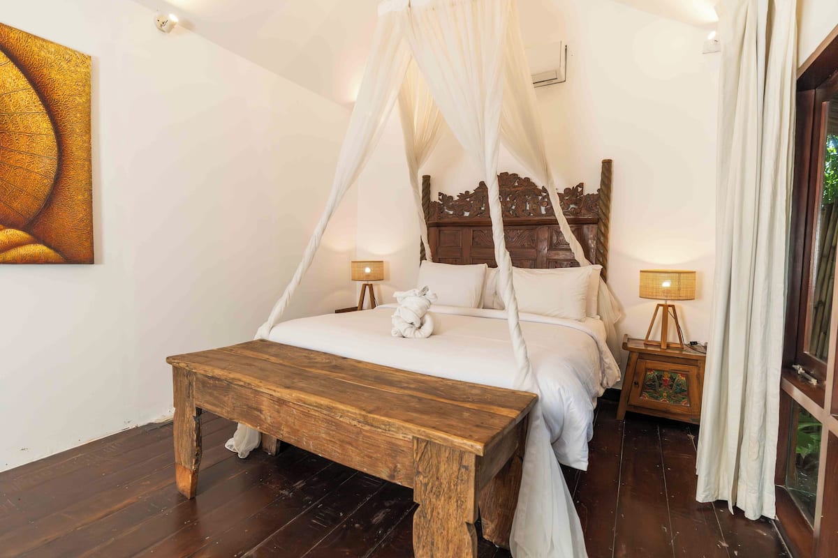 A bedroom with a four-poster bed, wooden bedside tables, and a large painting on the wall.