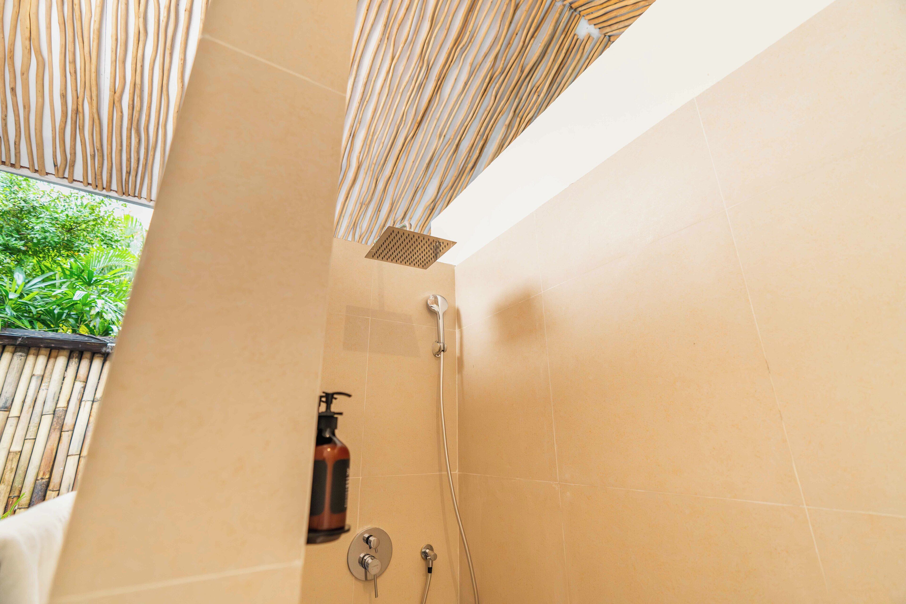 A bathroom with a shower, a bottle of shampoo, and a wooden slat ceiling.