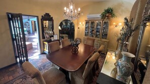 A dining room with a large wooden table, several chairs, a chandelier, and a cabinet with glass doors.