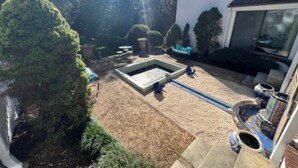 A garden with a rectangular pool, surrounded by trimmed bushes and trees.