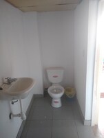 Un baño pequeño y blanco con lavamanos, inodoro y un cubo de basura.