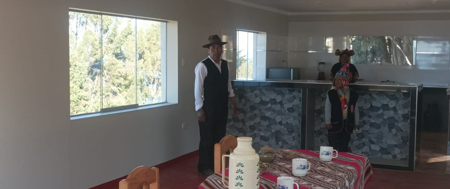 Comedor con una mesa preparada para dos, cocina con salpicadero de piedra y ventanas grandes que ofrecen vistas a árboles.