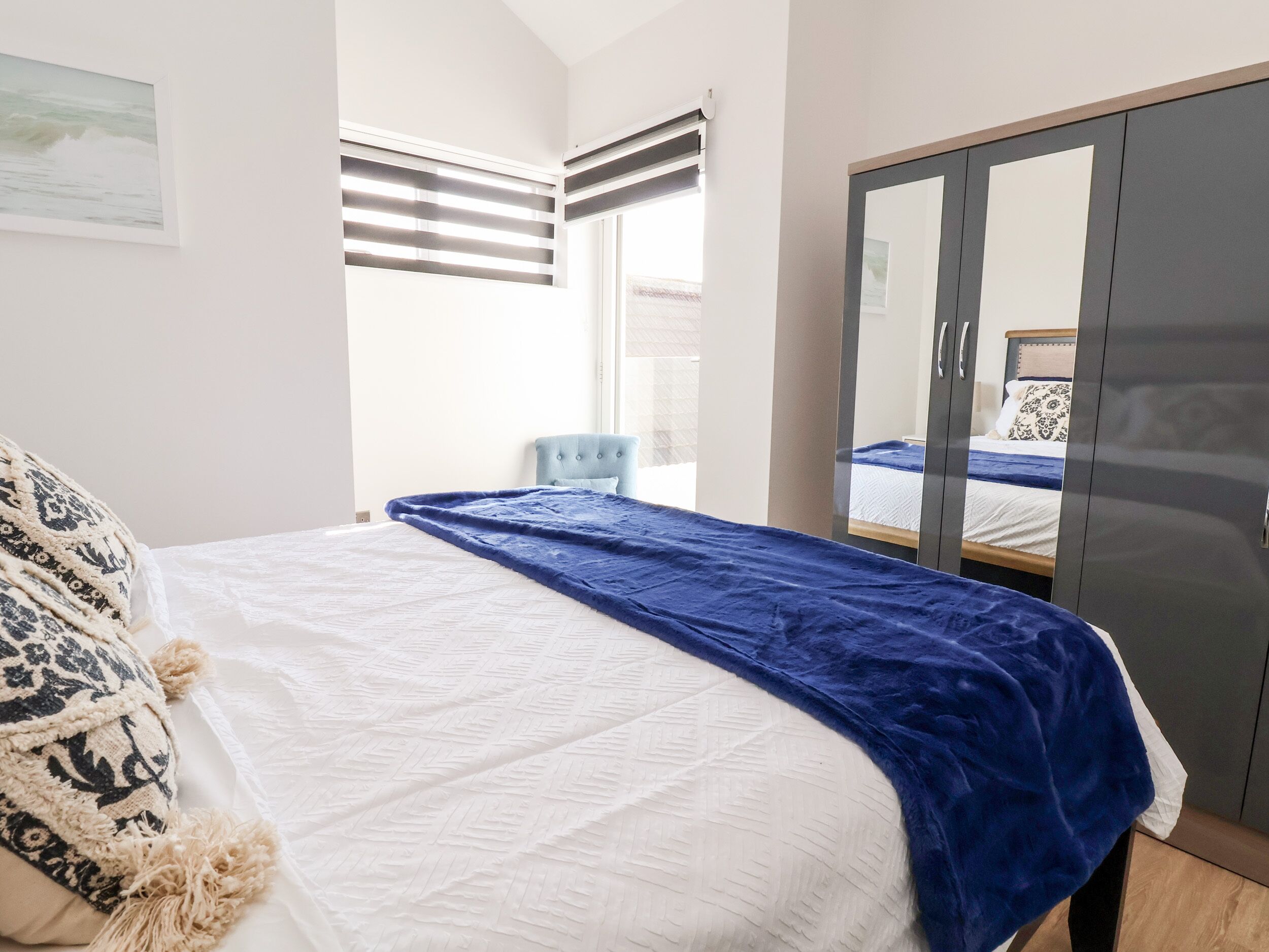 Une chambre à coucher avec un lit, une armoire, une chaise et une fenêtre avec des stores.