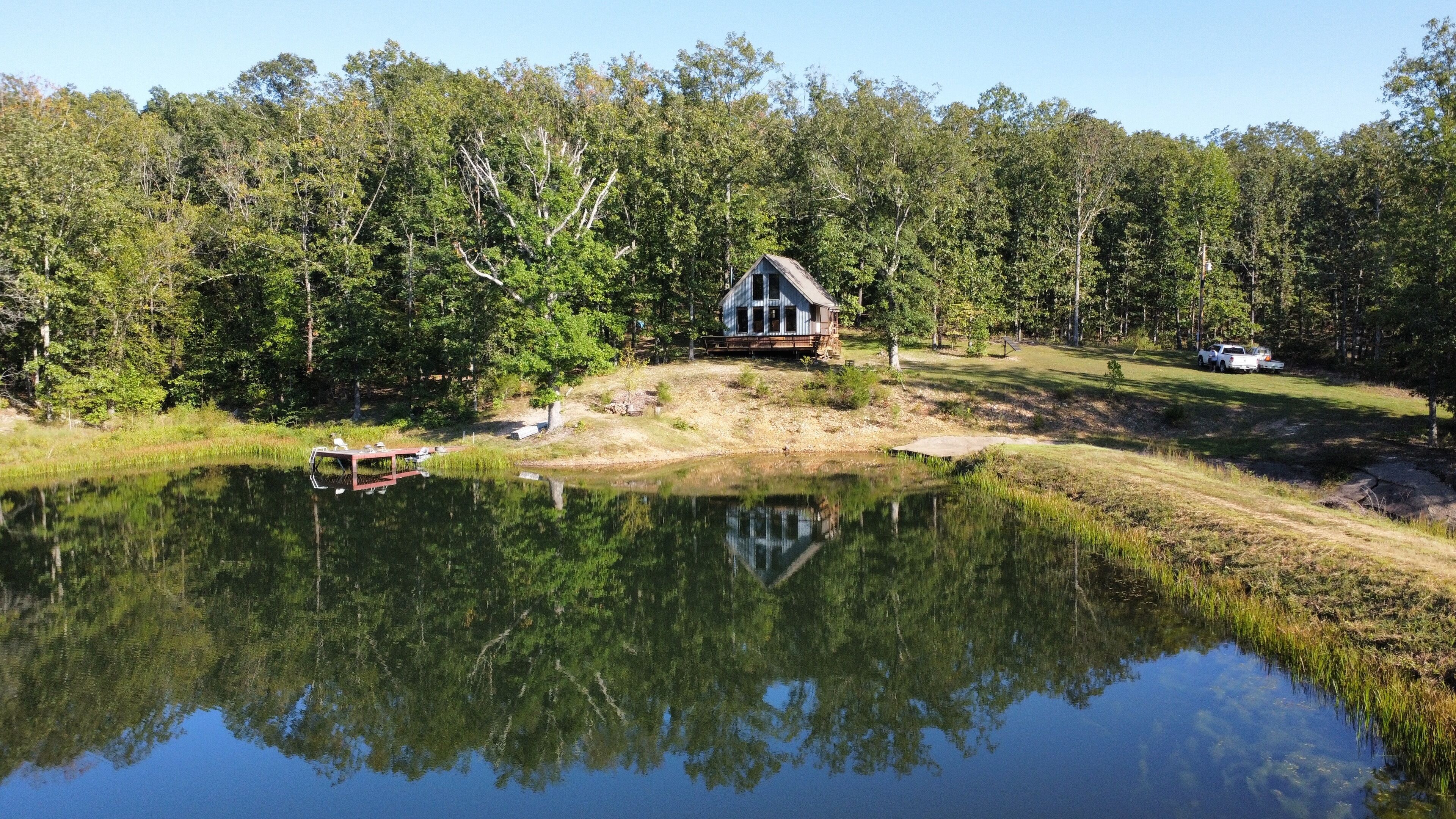 A cabin with a dock, surrounded by a forest and a pond.
