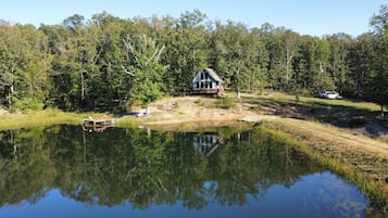 A cabin with a dock, surrounded by a forest and a pond.