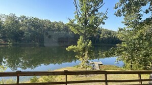 Una terrassa de fusta amb una banca que dona a un llac tranquil, envoltada d'arbres i un moll amb una barca.