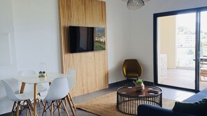 A modern living room with a dining area, a sofa, a coffee table, and a TV mounted on the wall. - Appartement 2 Pièces Porto Vecchio (Porto-Vecchio)