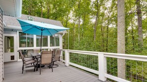 A covered outdoor deck with a table and chairs, surrounded by a white railing and a view of a forest. - Blue Ridge Mountain Retreat: Deck & Sunroom! (Fletcher)
