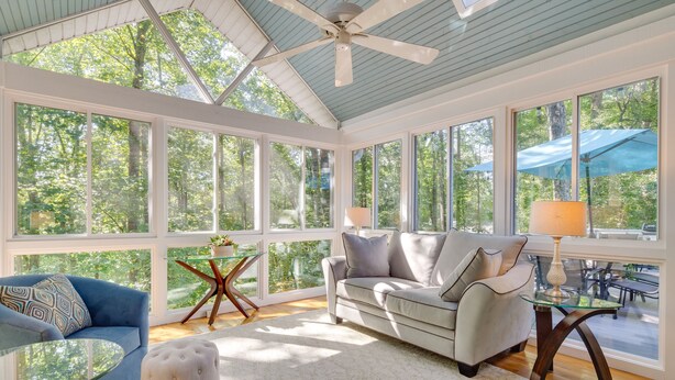 A sunroom with large windows, a ceiling fan, a sofa, a coffee table, and a lamp. - Blue Ridge Mountain Retreat: Deck & Sunroom! (Fletcher)