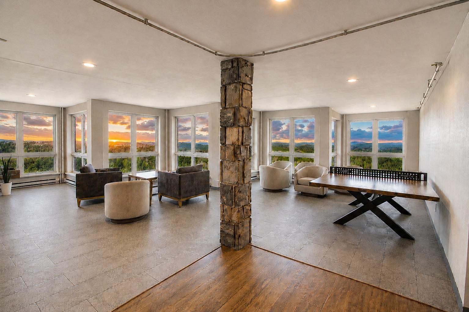 A spacious room with a ping pong table, multiple seating areas, and large windows offering a view of the landscape.