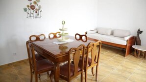 A dining area with a wooden table and chairs, a decorative wall piece, and a white sofa in the background.