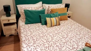 A neatly made bed with floral bedding, a teal headboard, and multiple pillows. There are two bedside tables with lamps. - Casa Maria (Penalva do Castelo)