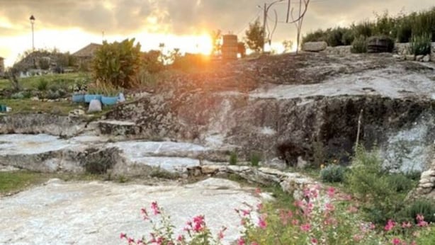 A stone structure with steps leading up to a platform, surrounded by greenery and flowers. - Casa Maria (Penalva do Castelo)