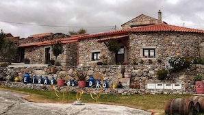 A stone building with a red-tiled roof, a stone wall, and a sign with the name "EIRAS DO DÃO". - Casa Maria (Penalva do Castelo)