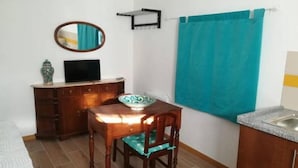A compact room with a wooden desk, a chair, a television on a cabinet, a mirror, and a blue towel hanging on the wall. - Casa Maria (Penalva do Castelo)