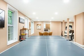 A ping pong table in a room with beige walls, a window, and a small table with cushions.